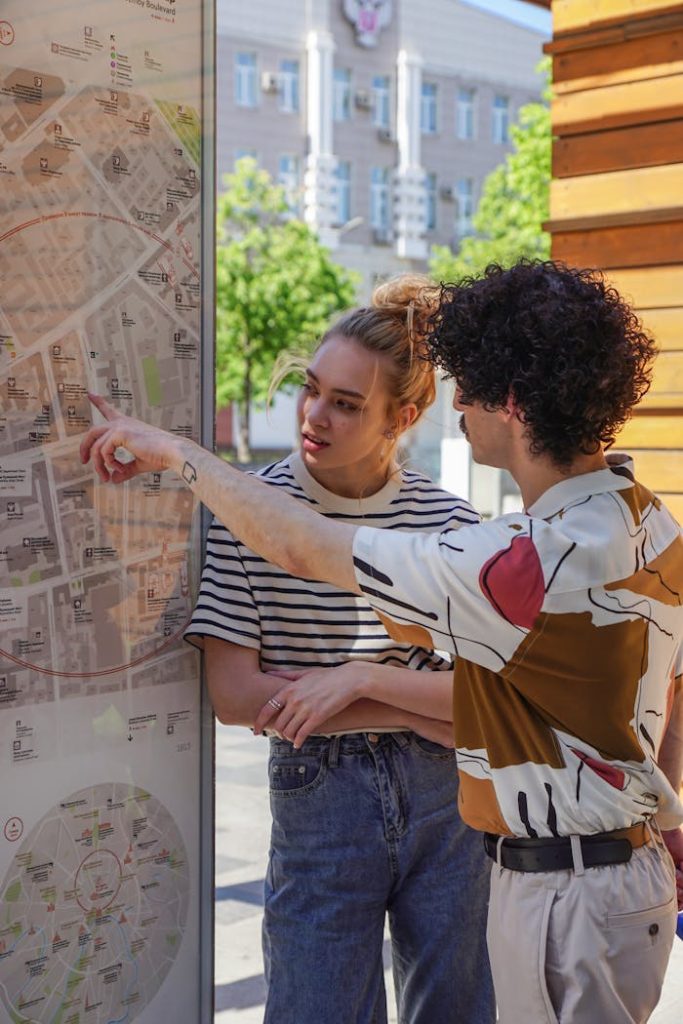 A couple examines a city map outdoors on a sunny day, pointing at destinations.